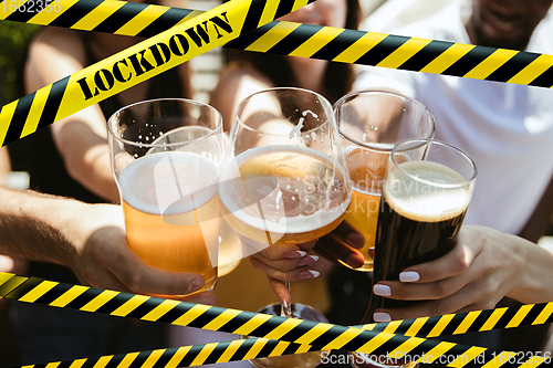 Image of Close up hands clinking glasses of beer at bar with bounding tapes Lockdown, Coronavirus, Quarantine, Warning - closing bars and nightclubs during pandemic