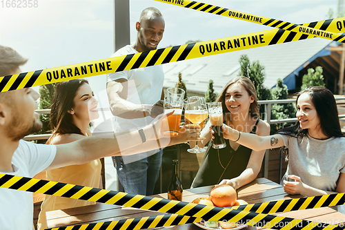 Image of Group of friends clinking glasses of beer at bar with bounding tapes Lockdown, Coronavirus, Quarantine, Warning - closing bars and nightclubs during pandemic