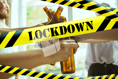 Image of Close up hands clinking bottles of beer at bar with bounding tapes Lockdown, Coronavirus, Quarantine, Warning - closing bars and nightclubs during pandemic