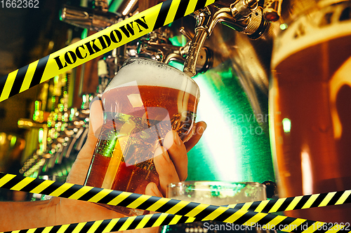 Image of Hand of bartender pouring a beer in tap with bounding tapes Lockdown, Coronavirus, Quarantine, Warning - closing bars and nightclubs during pandemic