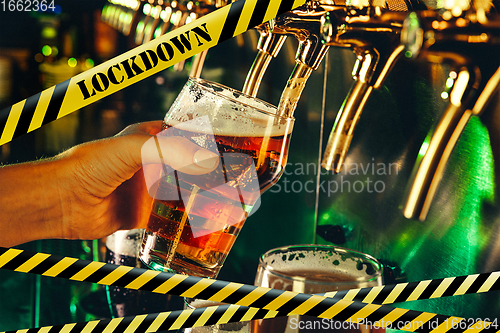 Image of Hand of bartender pouring a beer in tap with bounding tapes Lockdown, Coronavirus, Quarantine, Warning - closing bars and nightclubs during pandemic