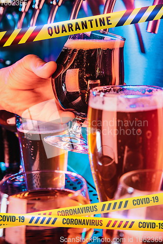 Image of Hand of bartender pouring a beer in tap with bounding tapes Lockdown, Coronavirus, Quarantine, Warning - closing bars and nightclubs during pandemic