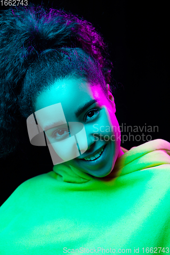 Image of African-american woman\'s portrait isolated on dark studio background in multicolored neon light