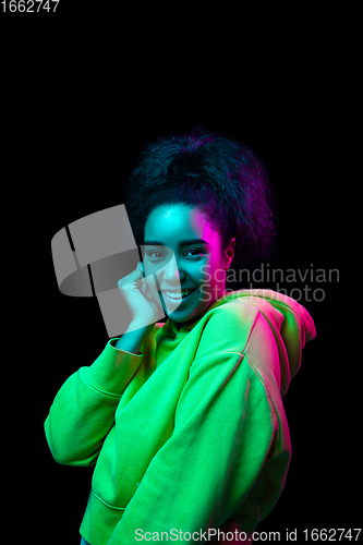 Image of African-american woman\'s portrait isolated on dark studio background in multicolored neon light