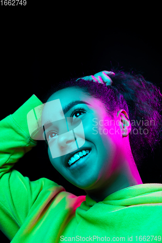 Image of African-american woman\'s portrait isolated on dark studio background in multicolored neon light