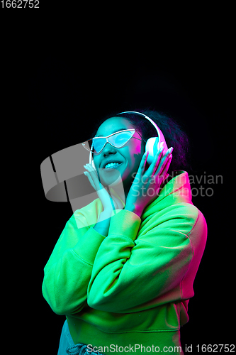 Image of African-american woman\'s portrait isolated on dark studio background in multicolored neon light