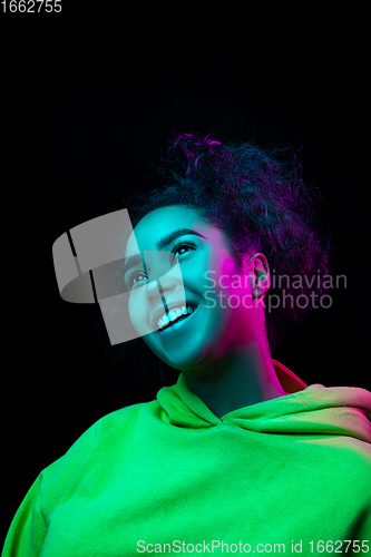 Image of African-american woman\'s portrait isolated on dark studio background in multicolored neon light