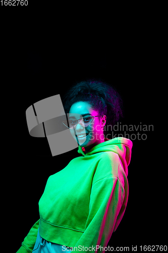 Image of African-american woman\'s portrait isolated on dark studio background in multicolored neon light