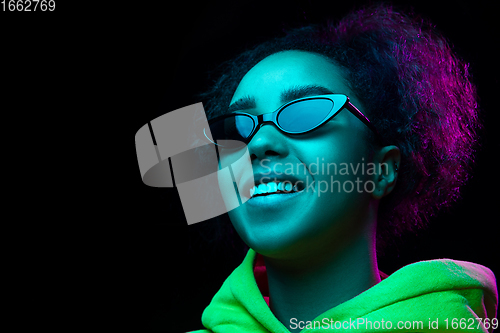 Image of African-american woman\'s portrait isolated on dark studio background in multicolored neon light