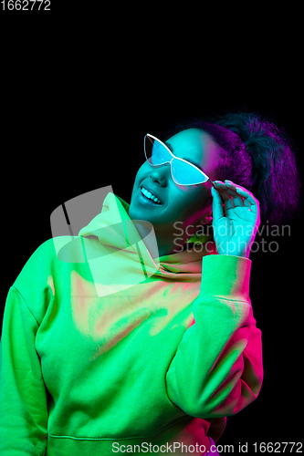 Image of African-american woman\'s portrait isolated on dark studio background in multicolored neon light