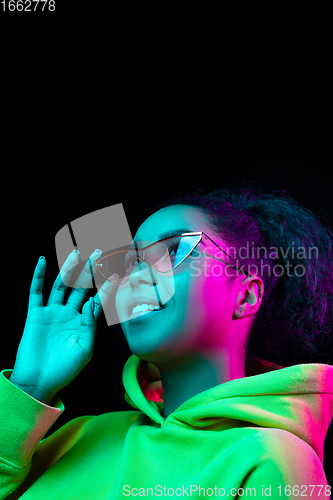 Image of African-american woman\'s portrait isolated on dark studio background in multicolored neon light