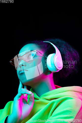 Image of African-american woman\'s portrait isolated on dark studio background in multicolored neon light