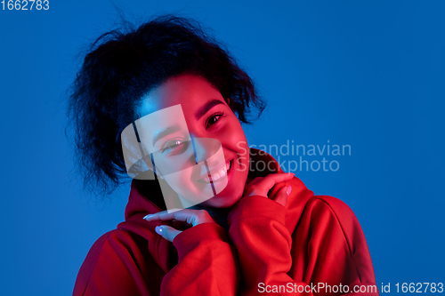 Image of African-american woman\'s portrait isolated on blue studio background in multicolored neon light