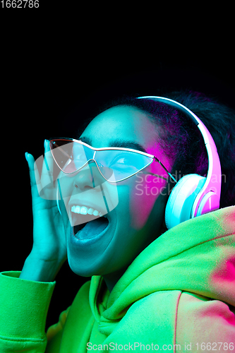 Image of African-american woman\'s portrait isolated on dark studio background in multicolored neon light