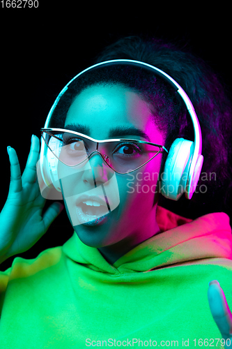 Image of African-american woman\'s portrait isolated on dark studio background in multicolored neon light