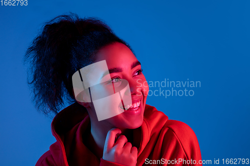 Image of African-american woman\'s portrait isolated on blue studio background in multicolored neon light