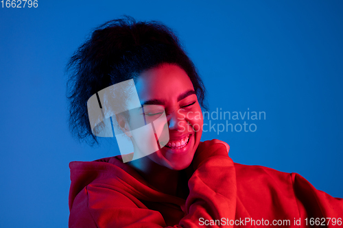 Image of African-american woman\'s portrait isolated on blue studio background in multicolored neon light