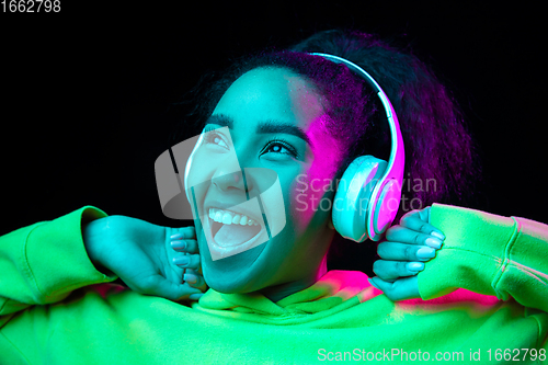 Image of African-american woman\'s portrait isolated on dark studio background in multicolored neon light