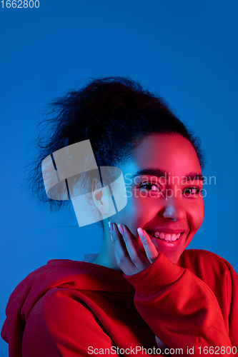 Image of African-american woman\'s portrait isolated on blue studio background in multicolored neon light