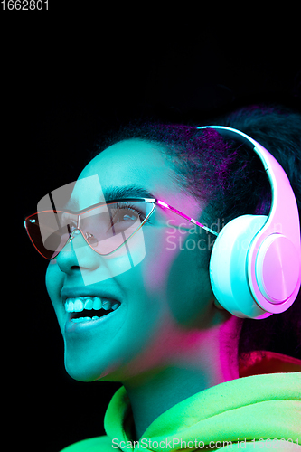 Image of African-american woman\'s portrait isolated on dark studio background in multicolored neon light