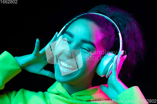 Image of African-american woman\'s portrait isolated on dark studio background in multicolored neon light