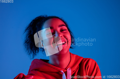 Image of African-american woman\'s portrait isolated on blue studio background in multicolored neon light