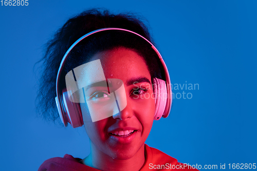 Image of African-american woman\'s portrait isolated on blue studio background in multicolored neon light