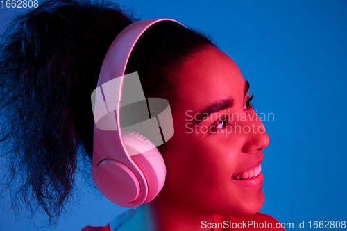 Image of African-american woman\'s portrait isolated on blue studio background in multicolored neon light