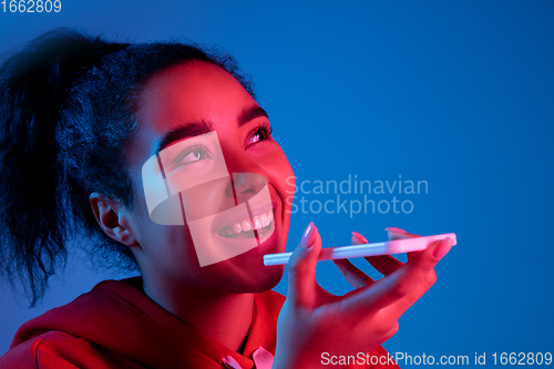 Image of African-american woman\'s portrait isolated on blue studio background in multicolored neon light
