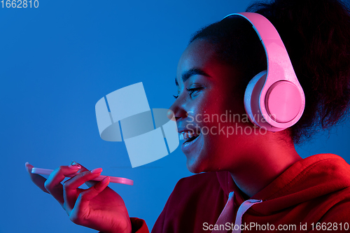 Image of African-american woman\'s portrait isolated on blue studio background in multicolored neon light