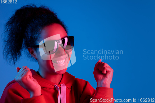 Image of African-american woman\'s portrait isolated on blue studio background in multicolored neon light