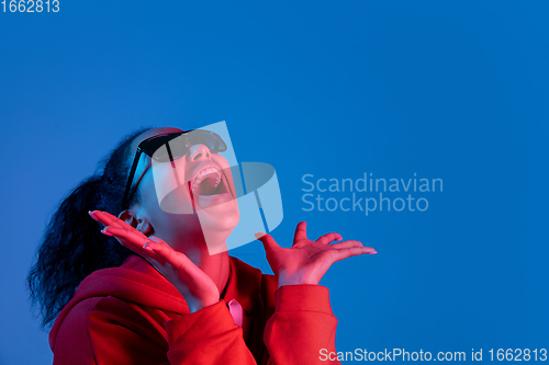 Image of African-american woman\'s portrait isolated on blue studio background in multicolored neon light