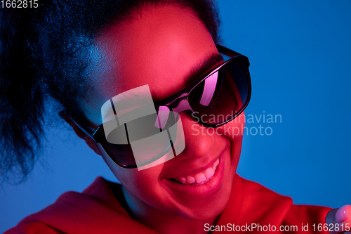 Image of African-american woman\'s portrait isolated on blue studio background in multicolored neon light