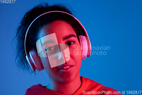 Image of African-american woman\'s portrait isolated on blue studio background in multicolored neon light