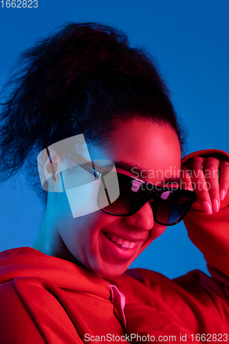 Image of African-american woman\'s portrait isolated on blue studio background in multicolored neon light