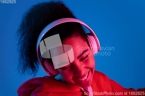 Image of African-american woman\'s portrait isolated on blue studio background in multicolored neon light