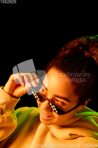 Image of African-american woman\'s portrait isolated on dark studio background in multicolored neon light