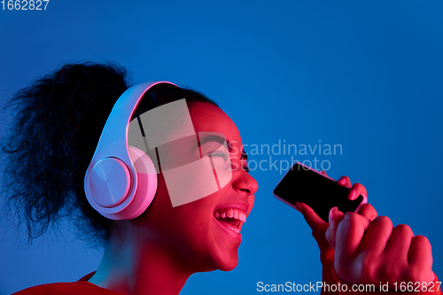 Image of African-american woman\'s portrait isolated on blue studio background in multicolored neon light