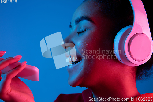 Image of African-american woman\'s portrait isolated on blue studio background in multicolored neon light