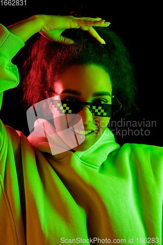 Image of African-american woman\'s portrait isolated on dark studio background in multicolored neon light