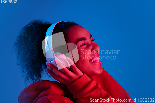 Image of African-american woman\'s portrait isolated on blue studio background in multicolored neon light