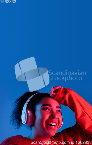 Image of African-american woman\'s portrait isolated on blue studio background in multicolored neon light