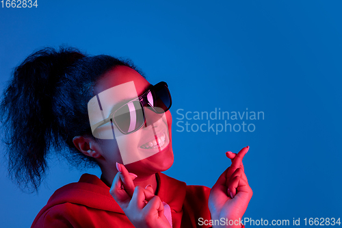 Image of African-american woman\'s portrait isolated on blue studio background in multicolored neon light