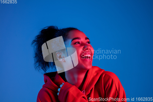 Image of African-american woman\'s portrait isolated on blue studio background in multicolored neon light