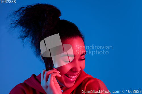 Image of African-american woman\'s portrait isolated on blue studio background in multicolored neon light