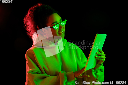 Image of African-american woman\'s portrait isolated on dark studio background in multicolored neon light