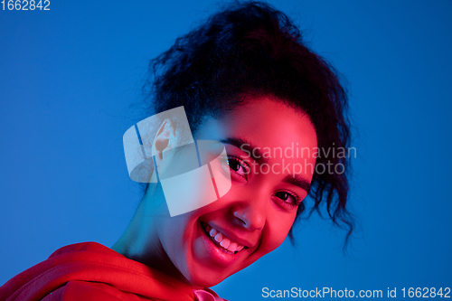 Image of African-american woman\'s portrait isolated on blue studio background in multicolored neon light