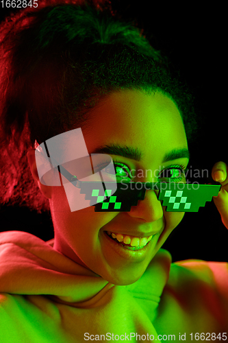 Image of African-american woman\'s portrait isolated on dark studio background in multicolored neon light