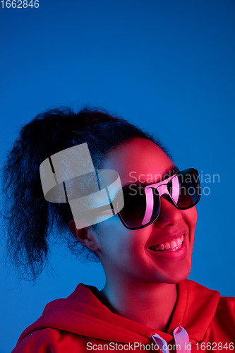 Image of African-american woman\'s portrait isolated on blue studio background in multicolored neon light