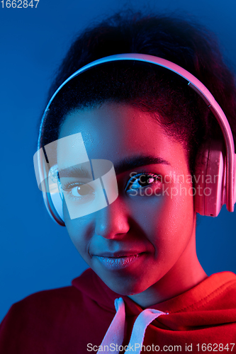 Image of African-american woman\'s portrait isolated on blue studio background in multicolored neon light